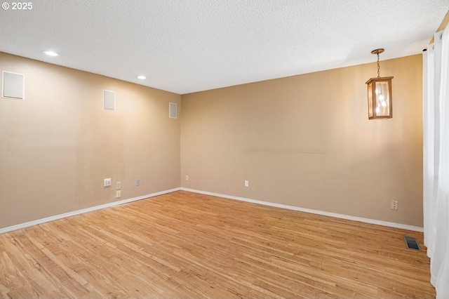 spare room featuring visible vents, a textured ceiling, baseboards, and light wood-style floors