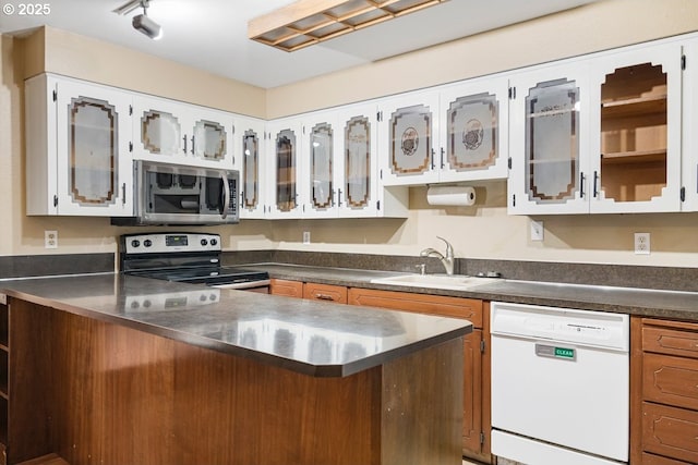 kitchen with a sink, stainless steel counters, stainless steel appliances, a peninsula, and glass insert cabinets