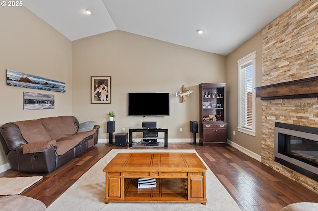 living area featuring wood finished floors, vaulted ceiling, a stone fireplace, baseboards, and recessed lighting