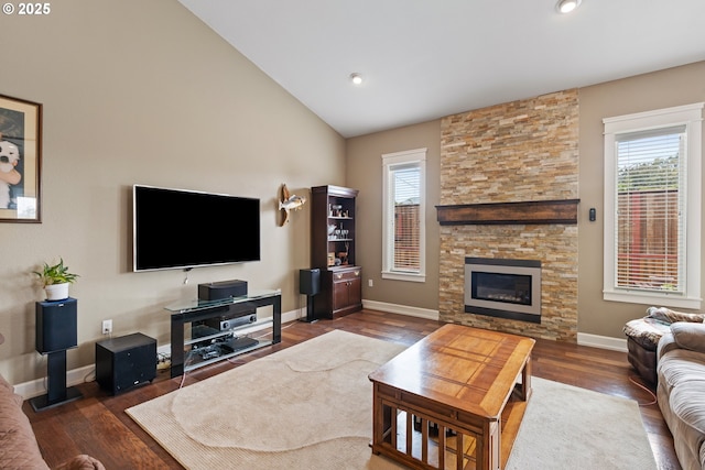living area featuring healthy amount of natural light, wood finished floors, a stone fireplace, baseboards, and lofted ceiling
