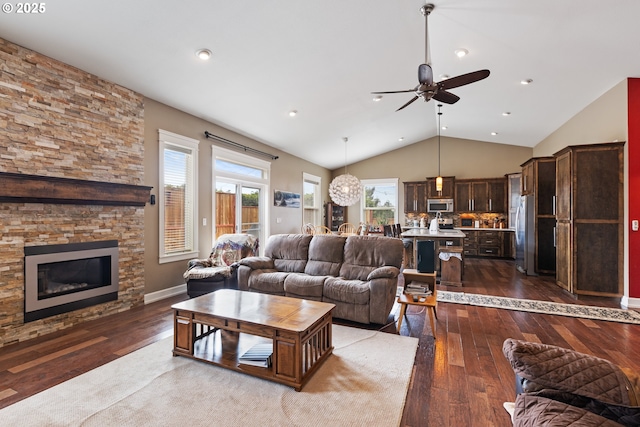 living room with ceiling fan, dark wood finished floors, vaulted ceiling, and a stone fireplace