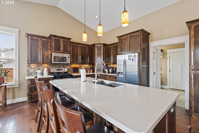 kitchen with appliances with stainless steel finishes, a sink, tasteful backsplash, dark brown cabinets, and high vaulted ceiling