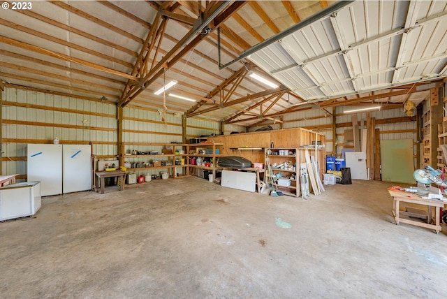 garage with freestanding refrigerator, a workshop area, and metal wall