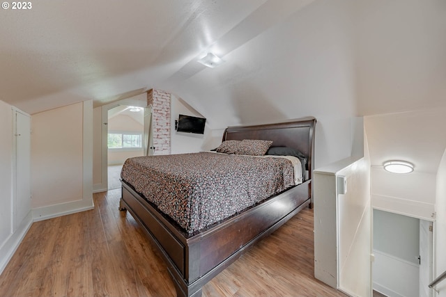 bedroom featuring baseboards, vaulted ceiling, and light wood-type flooring