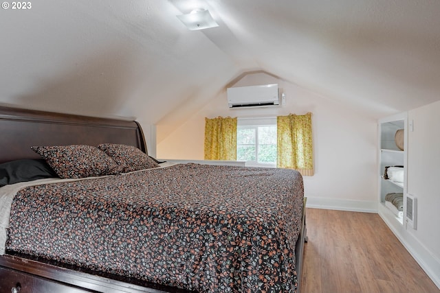 bedroom with an AC wall unit, baseboards, vaulted ceiling, and wood finished floors