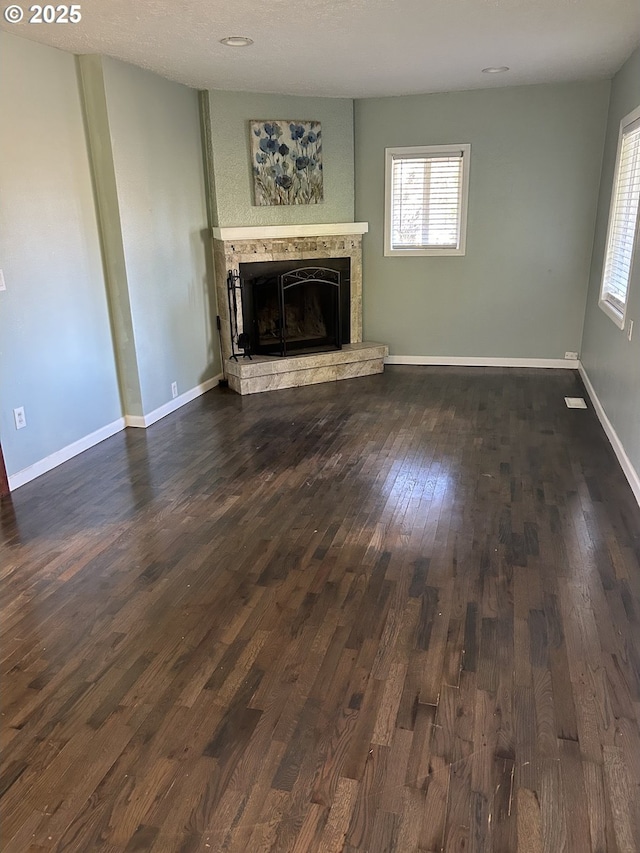 unfurnished living room with baseboards, a fireplace with raised hearth, and dark wood-style flooring