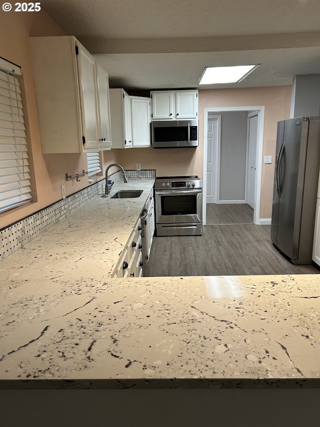 kitchen featuring light stone counters, wood finished floors, stainless steel appliances, white cabinetry, and a sink