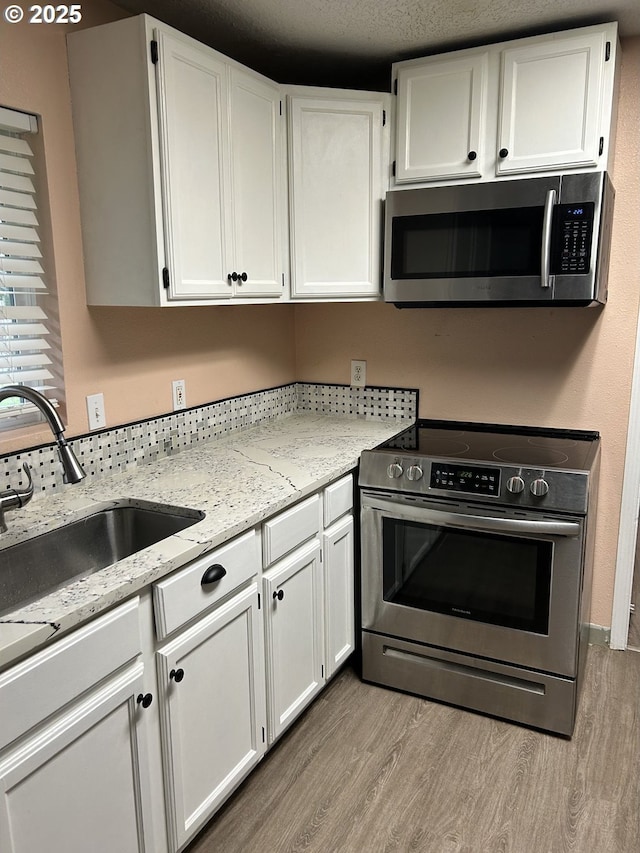 kitchen with stainless steel appliances, white cabinets, light wood finished floors, and light stone countertops