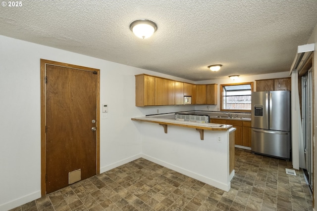 730 SW Dolph St, Portland, OR 97219 - kitchen with stainless steel fridge, a peninsula, brown cabinetry, a kitchen bar, and a textured ceiling