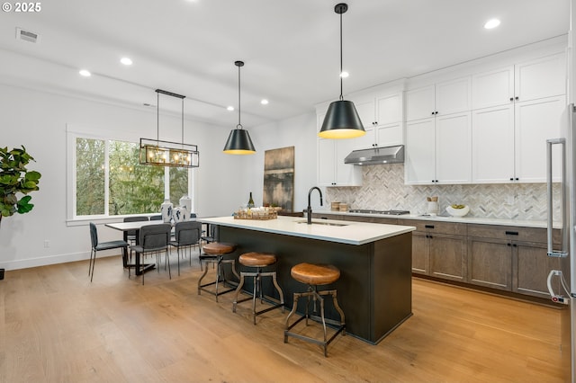 kitchen featuring hanging light fixtures, white cabinetry, sink, and a kitchen island with sink