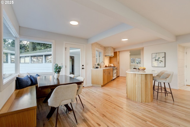 dining space featuring beam ceiling, light wood-type flooring, and sink