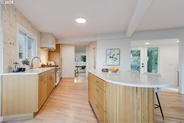 kitchen featuring white range with gas cooktop, light brown cabinets, a spacious island, and light wood-type flooring