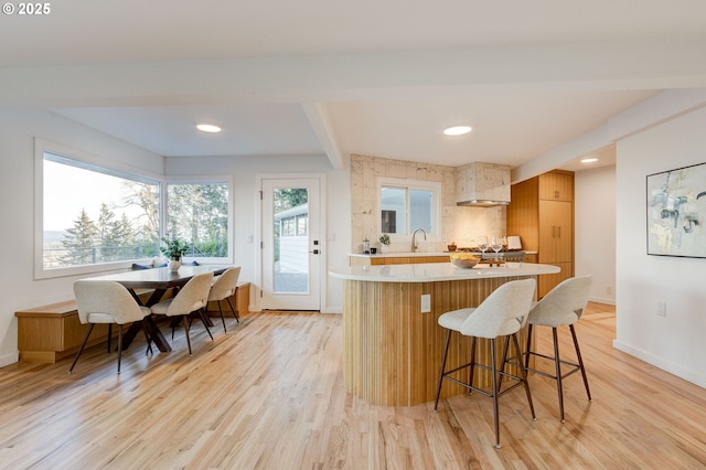 kitchen with beam ceiling, sink, backsplash, light hardwood / wood-style floors, and a breakfast bar