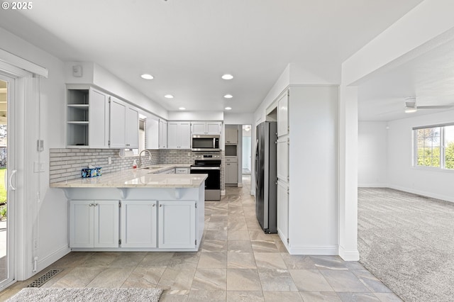 kitchen with a peninsula, a sink, appliances with stainless steel finishes, backsplash, and open shelves