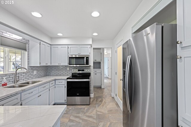 kitchen with stainless steel appliances, recessed lighting, tasteful backsplash, a sink, and light stone countertops