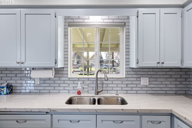 kitchen with light stone counters, a sink, and decorative backsplash