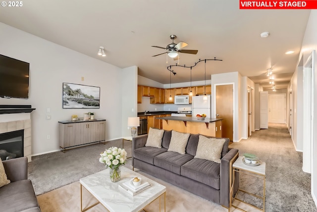 living room with a tiled fireplace, ceiling fan, light carpet, and lofted ceiling