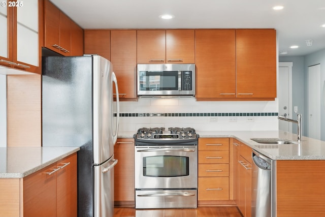 kitchen with light stone countertops, a peninsula, a sink, decorative backsplash, and stainless steel appliances