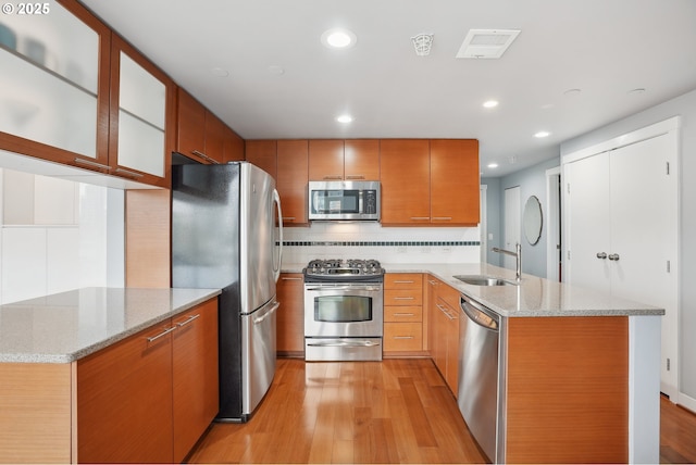 kitchen featuring light wood-style flooring, a sink, tasteful backsplash, stainless steel appliances, and a peninsula