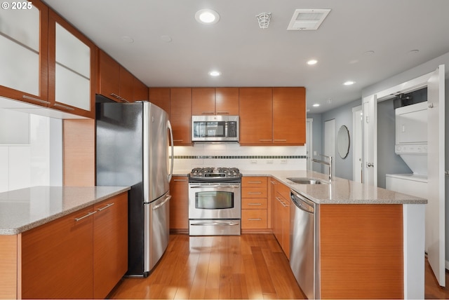 kitchen featuring a sink, stacked washing maching and dryer, stainless steel appliances, light wood-style floors, and a peninsula