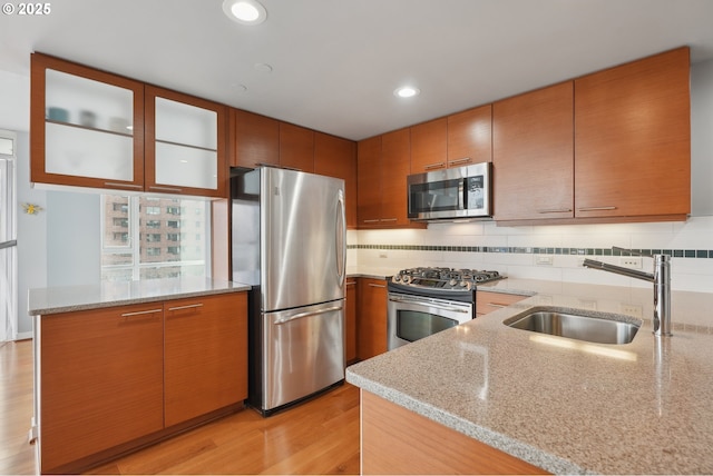 kitchen featuring light stone counters, backsplash, appliances with stainless steel finishes, and a sink