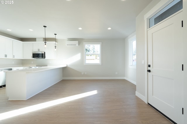 kitchen featuring pendant lighting, dishwasher, a wall mounted AC, light hardwood / wood-style floors, and white cabinets