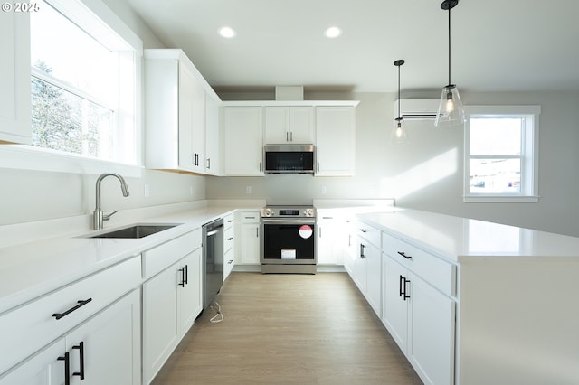 kitchen with sink, light hardwood / wood-style flooring, hanging light fixtures, stainless steel appliances, and white cabinets