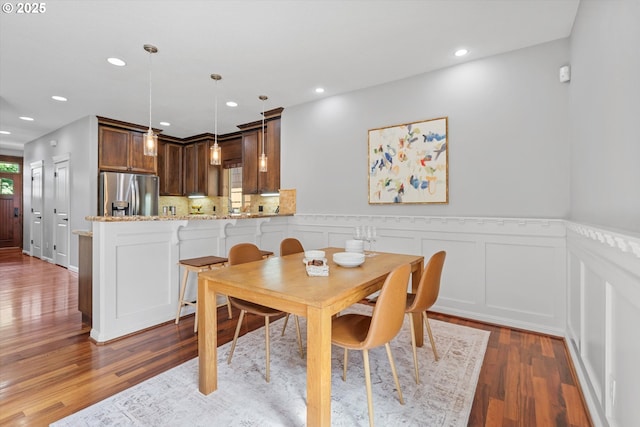 dining room with wood finished floors, wainscoting, recessed lighting, and a decorative wall