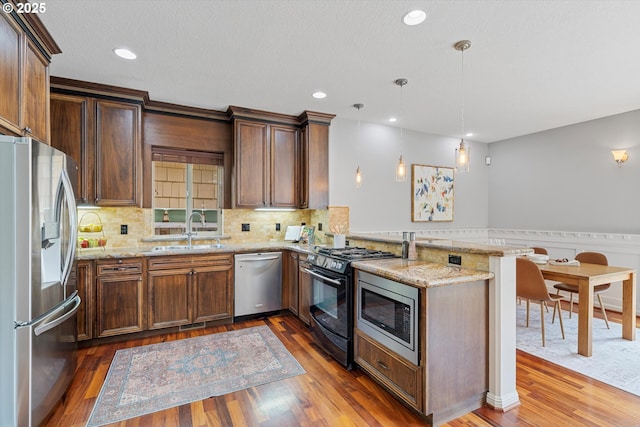 kitchen with stainless steel appliances, a sink, a peninsula, light stone counters, and recessed lighting