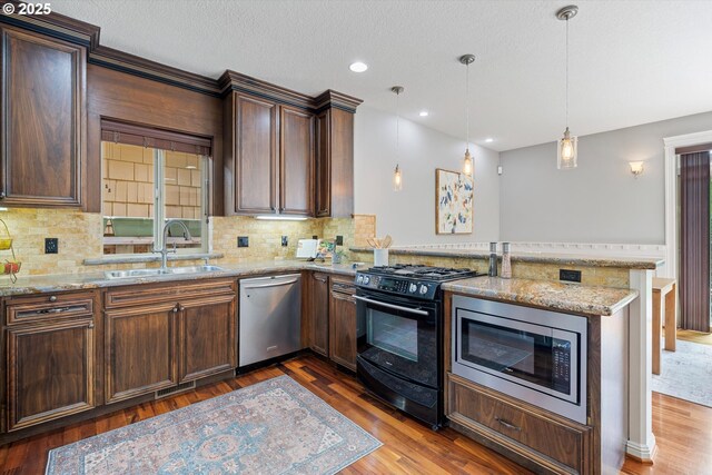 kitchen featuring stainless steel appliances, a sink, a peninsula, wood finished floors, and decorative backsplash