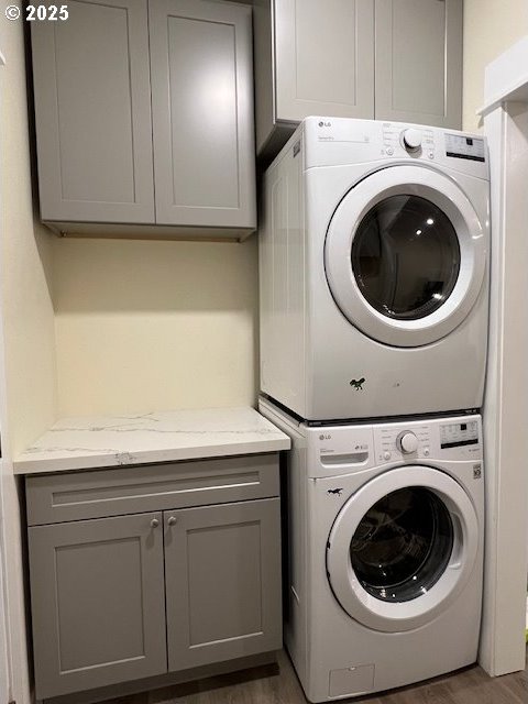 washroom featuring dark wood-type flooring, cabinets, and stacked washing maching and dryer