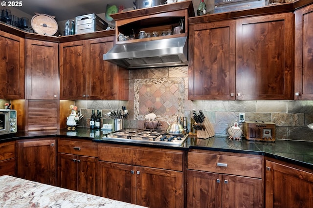 kitchen with wall chimney exhaust hood, stainless steel gas stovetop, a toaster, and backsplash