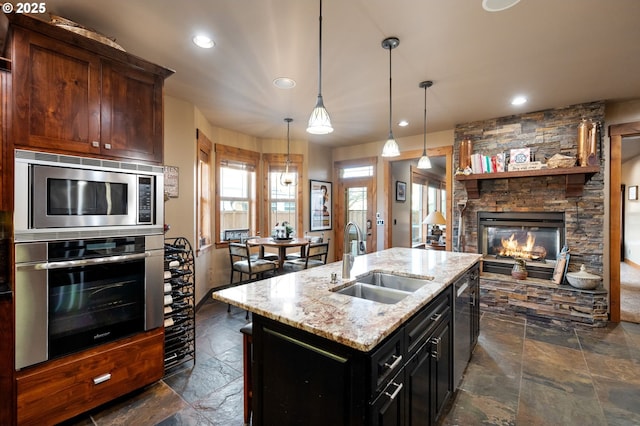 kitchen with appliances with stainless steel finishes, light stone countertops, stone tile flooring, a fireplace, and a sink