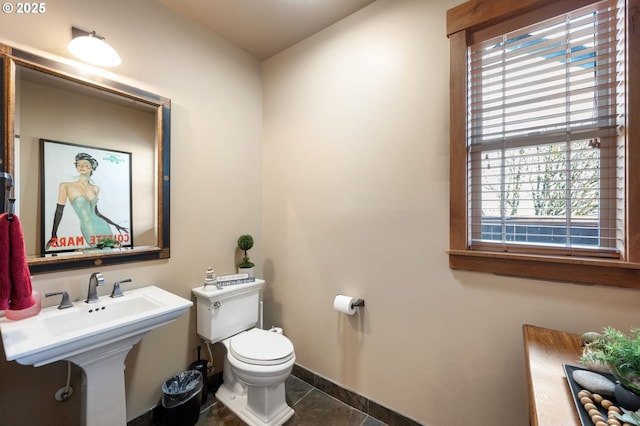 half bathroom with a sink, tile patterned flooring, toilet, and baseboards