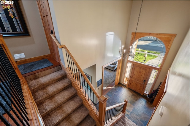 foyer with visible vents, a towering ceiling, stone finish floor, stairs, and a notable chandelier