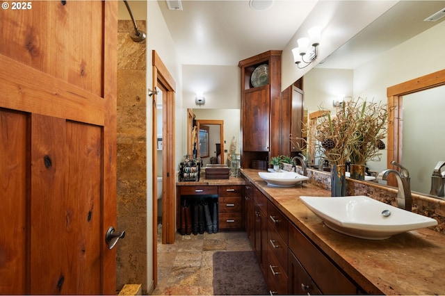 full bath featuring stone finish flooring, double vanity, a sink, and visible vents