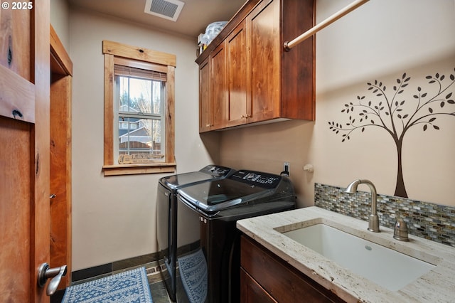 washroom with a sink, visible vents, baseboards, washer and dryer, and cabinet space