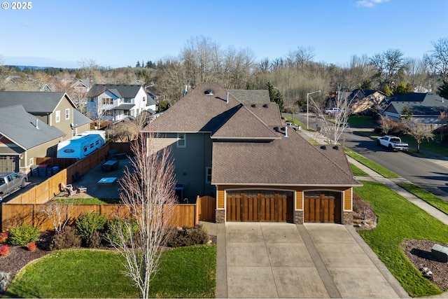 view of front of home featuring driveway, a shingled roof, stone siding, a residential view, and fence