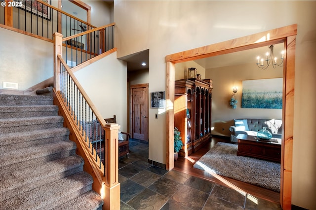 stairway with stone tile floors, visible vents, baseboards, a towering ceiling, and an inviting chandelier