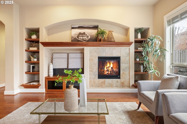 living area with a tile fireplace, hardwood / wood-style floors, and built in shelves