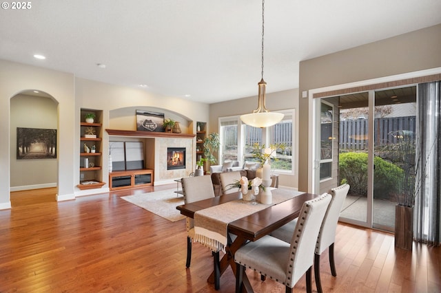 dining room with built in shelves, a fireplace, and hardwood / wood-style floors