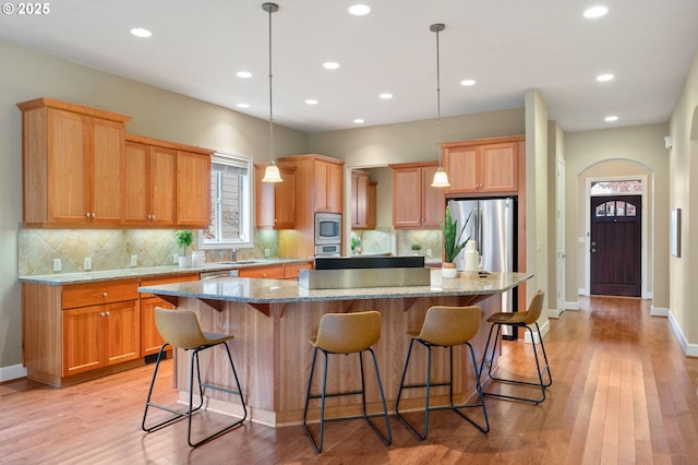 kitchen with pendant lighting, light stone counters, appliances with stainless steel finishes, and a kitchen island