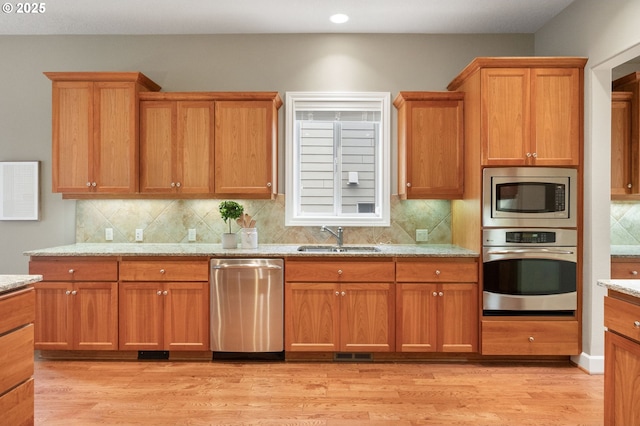 kitchen featuring appliances with stainless steel finishes, sink, backsplash, light stone counters, and light wood-type flooring