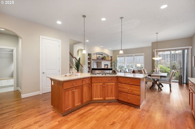 kitchen with light hardwood / wood-style floors, light stone countertops, hanging light fixtures, and a center island with sink