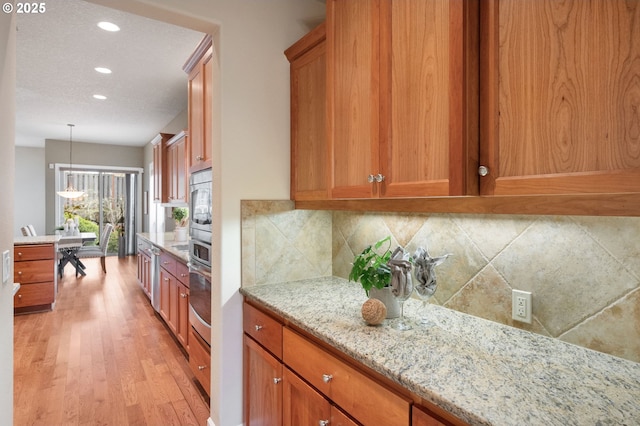 kitchen featuring tasteful backsplash, oven, hanging light fixtures, light stone countertops, and light hardwood / wood-style flooring