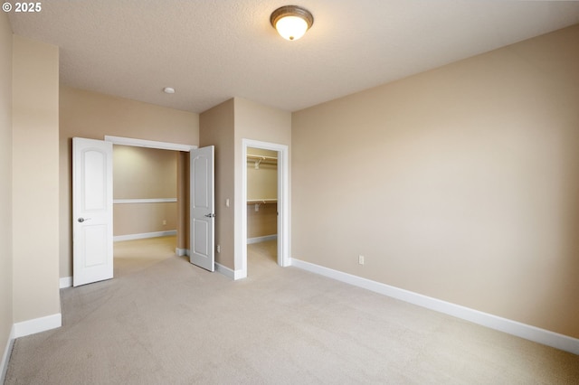 unfurnished bedroom with a closet, a spacious closet, light carpet, and a textured ceiling