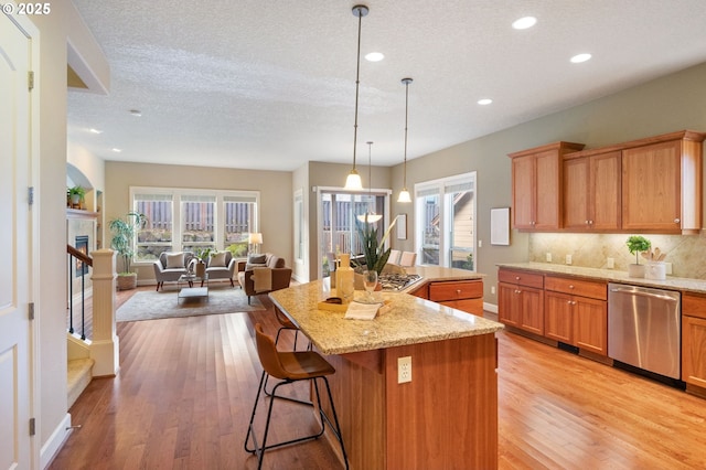 kitchen featuring appliances with stainless steel finishes, decorative light fixtures, a kitchen island, and light hardwood / wood-style flooring