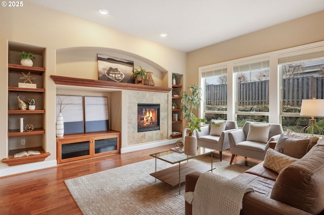 living room featuring built in shelves, wood-type flooring, and a tile fireplace