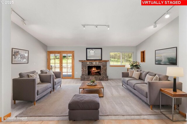 living room with a healthy amount of sunlight, a high end fireplace, rail lighting, and lofted ceiling