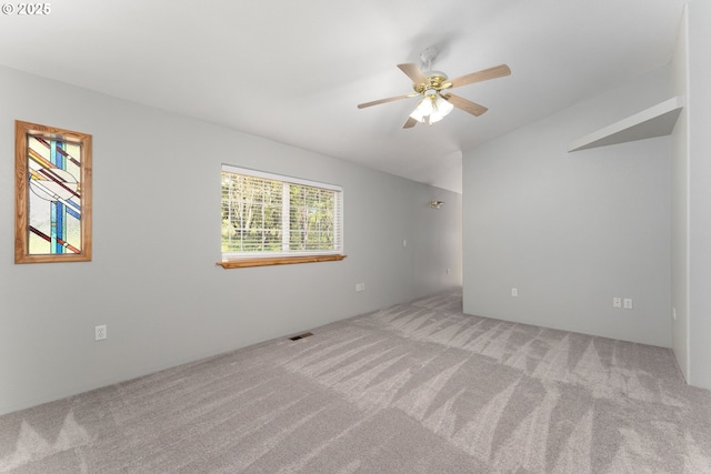 carpeted spare room featuring a ceiling fan, visible vents, and lofted ceiling